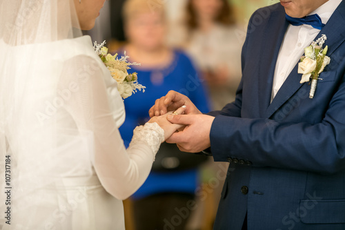 Young groom putting wedding ring on bride's finger