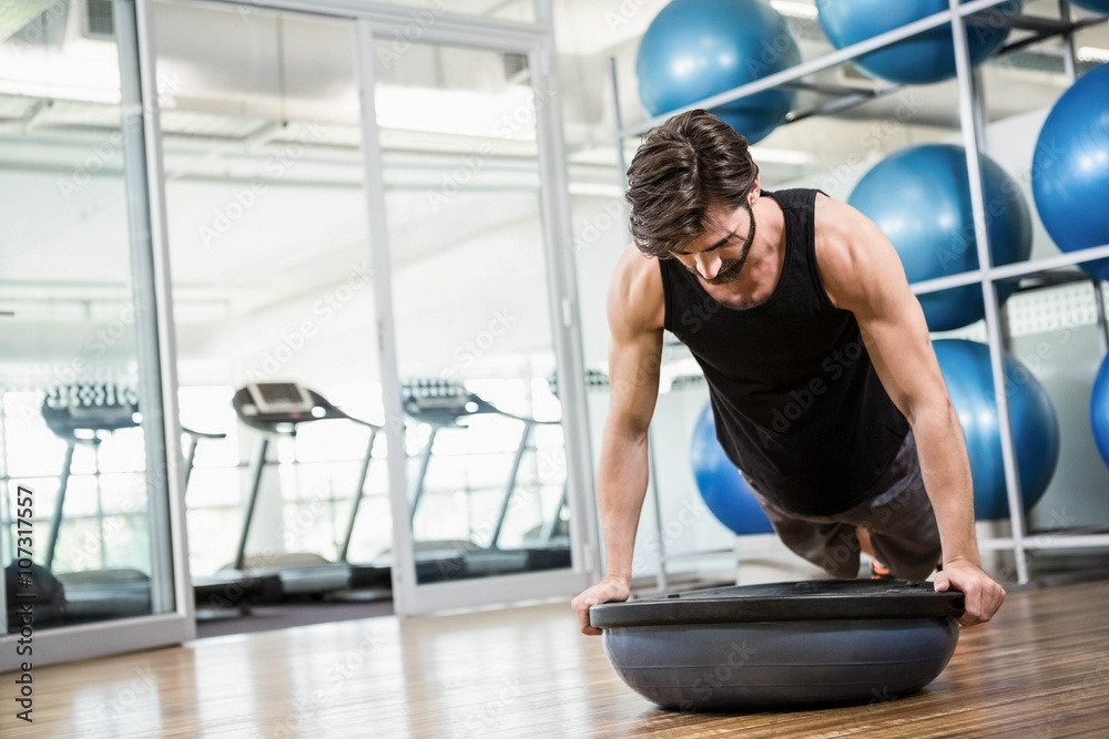 Fototapeta premium Serious man doing exercise with bosu ball in the studio