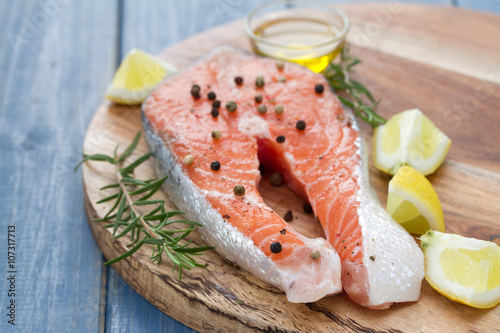 fresh salmon with lemon, oil and rosemary on wooden board on white background