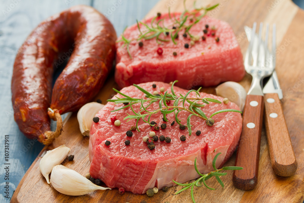 raw meat with smoked sausage, pepper and garlic on wooden board on blue background