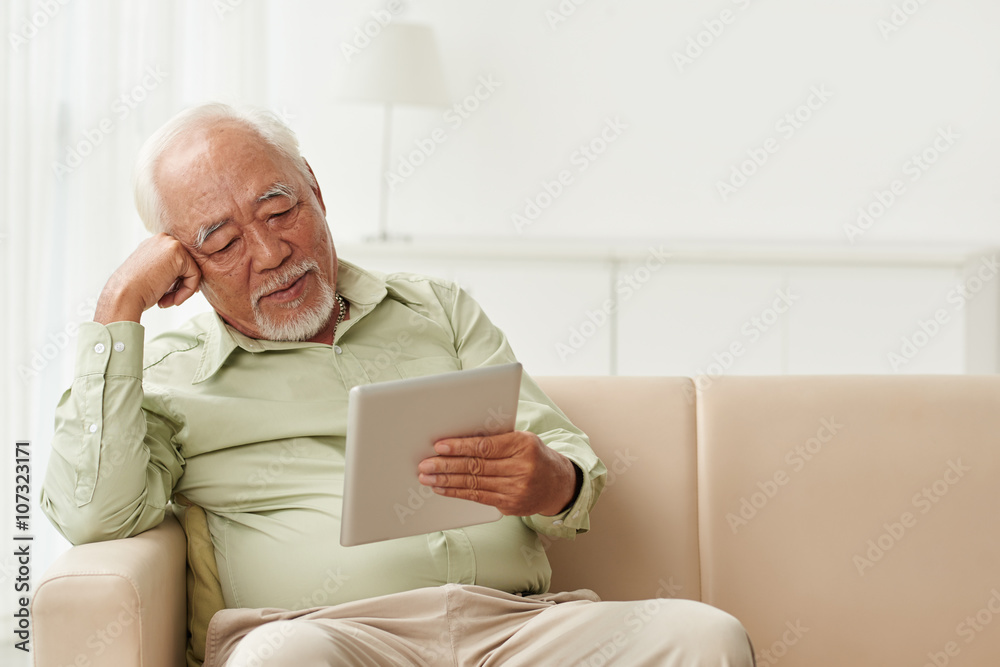 Old man reading book on tablet computer at home Old man reading book on tablet computer at home
