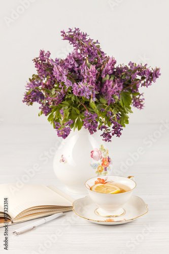 Tea with  lemon and bouquet of  lilac primroses on the table