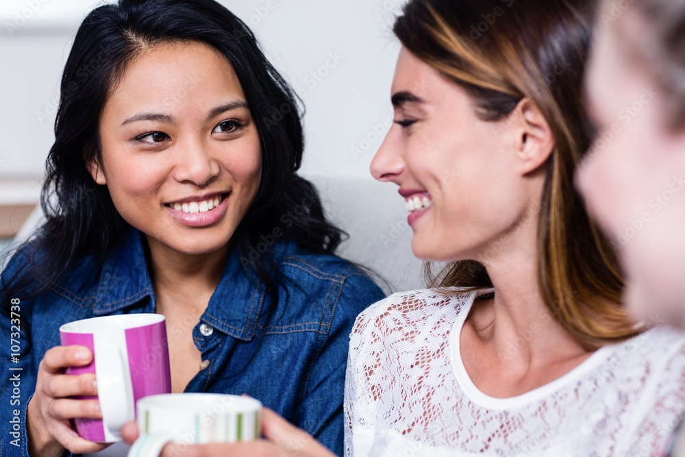 Happy female friends with coffee cup sitting on sofa Happy female friends with coffee cup sitting on sofa
