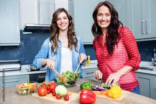 Portrait of smiling female friends preparing vegetable salad