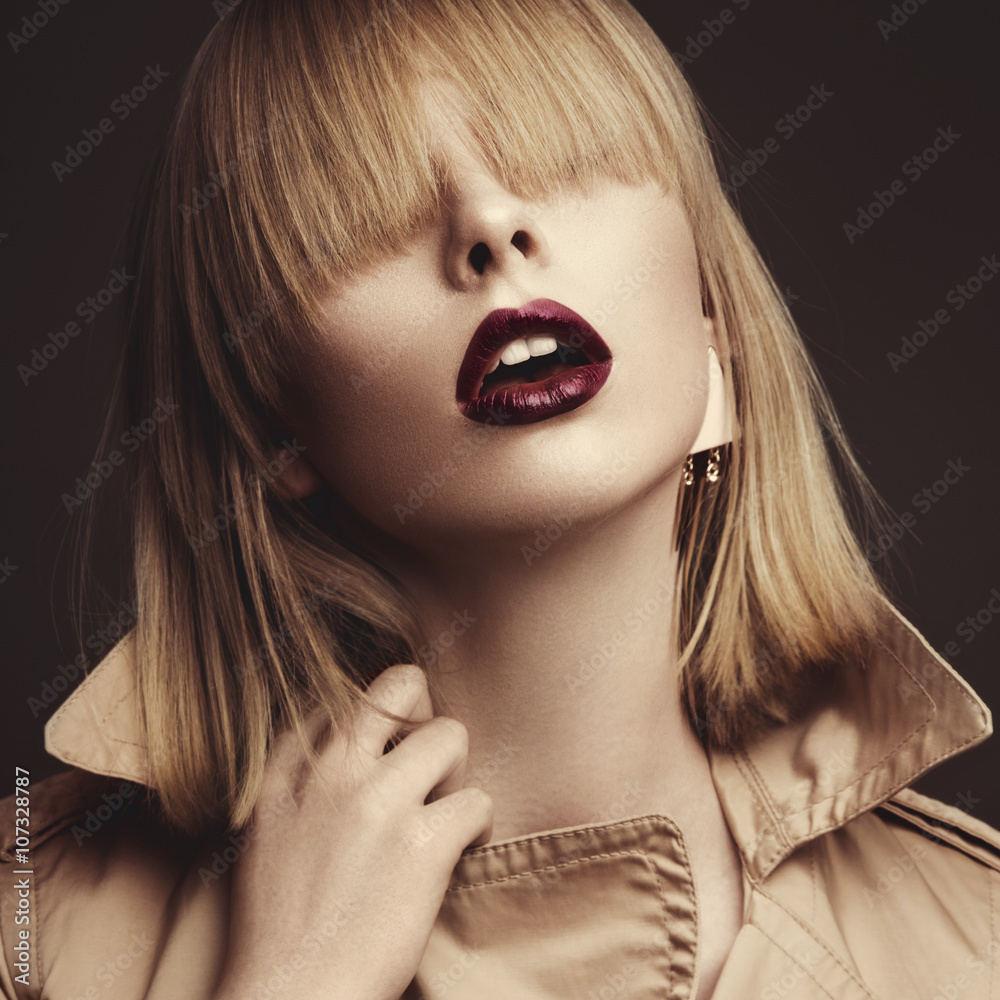 Fototapeta premium Beautiful blonde woman in a bright coat and dark lips, showing d