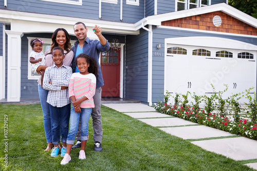 Happy black family standing outside their house, dad holding the