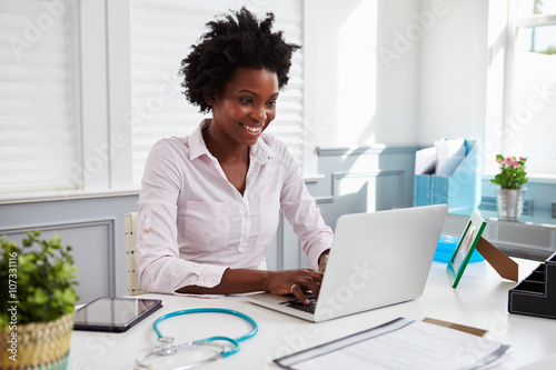 Black female doctor at work in office using laptop computer