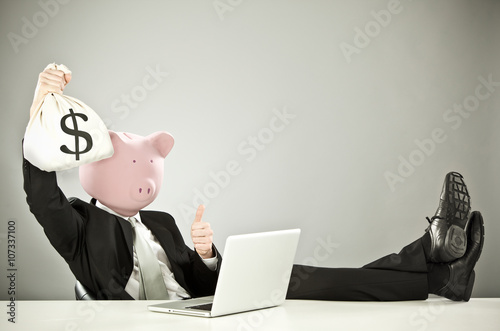 funny businessman with pig face hold money with laptop on grey background