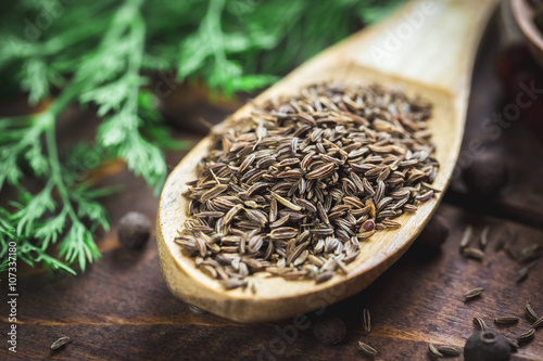 beautiful photo of cumin in wooden spoon on the background of the old wooden Desk and dill photo