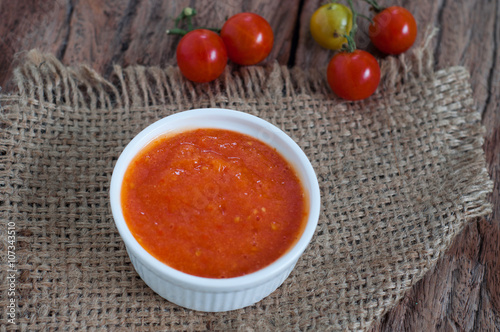 Homemade tomato sauce in white bowl on hemp sack with raw tomatoes