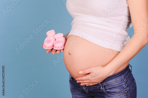 Pregnant woman holding baby shoes over blue closeup. Maternity. Motherhood. © morrowlight
