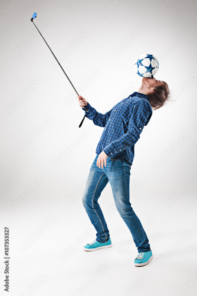The portrait of man with ball, holding selfie stick on white background