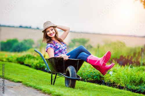 Schilderij op canvas Woman sitting in wheelbarrow in sunny green garden