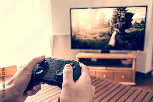 Playing game on console - hands holding game pad and playing shooter game on tv screen. photo