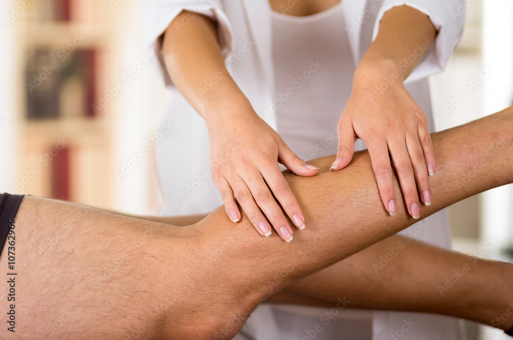 Obraz premium Closeup female physio therapist hands working on male patients legs, blurry clinic background