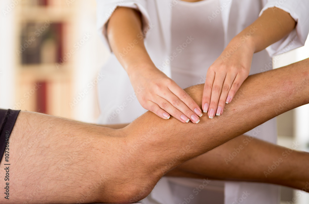 Obraz premium Closeup female physio therapist hands working on male patients legs, blurry clinic background