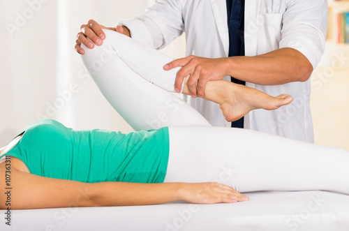Male physio therapist hands working on female patients legs  holding and bending  blurry clinic background