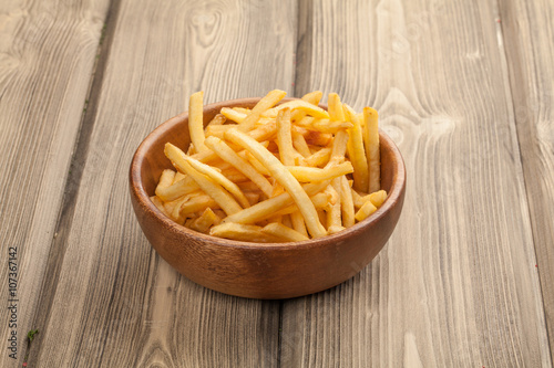 French fries in a wooden bowl, on a wooden background.