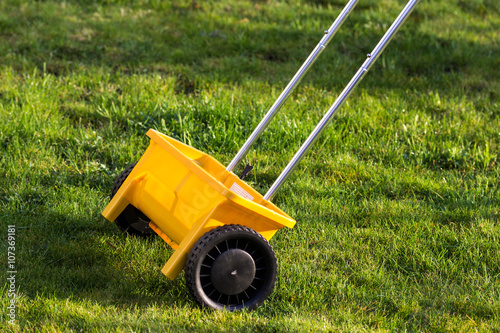 Rasen Gras düngen mit gelbem Streuwagen