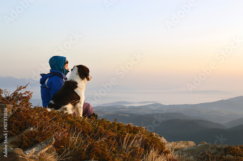 Young woman and dog admiring sunrise high in the mountain