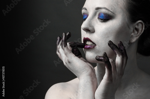 Beautiful woman with bright smoky eyes make-up, black and white skin and finger in the paint on a dark background