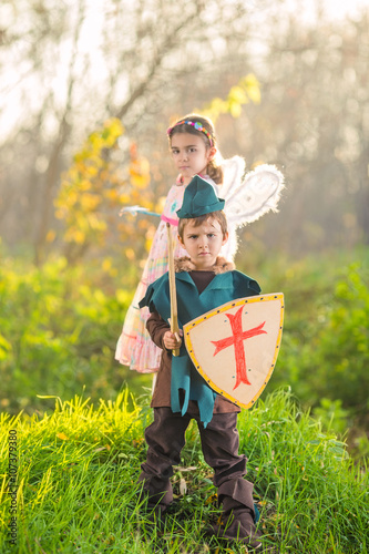 Cute little children dressed up as a knight and a fairy playing in the woods