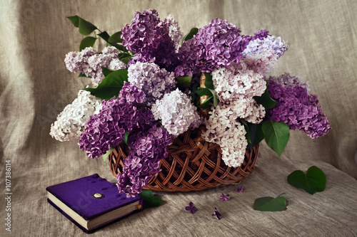 Still life: a lush bouquet of lilacs in a wicker basket and book on a linen background
