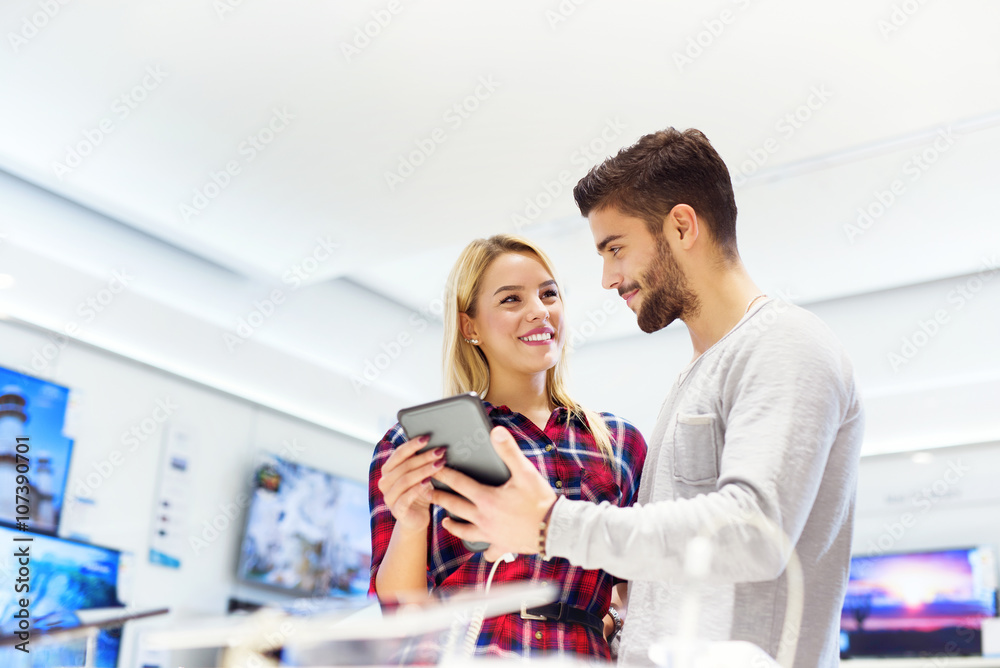 Lovely couple is at store and they are looking for a new tablet. They are taking selfie and smiling. Shallow depth of field.