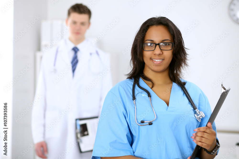 Female african american medical doctor with colleagues in background Female african american medical doctor with colleagues in background