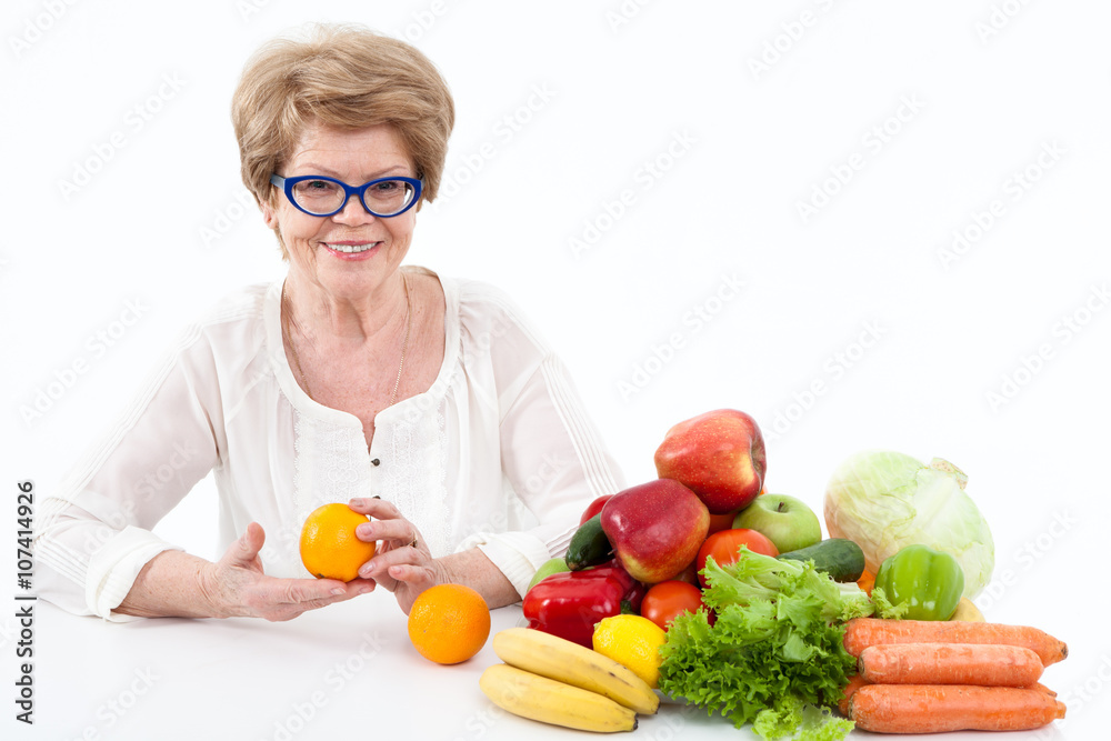 Smiling senior Caucasian woman holding hands two oranges, vegetables and fruits are on table, white background Smiling senior Caucasian woman holding hands two oranges, vegetables and fruits are on table, white background