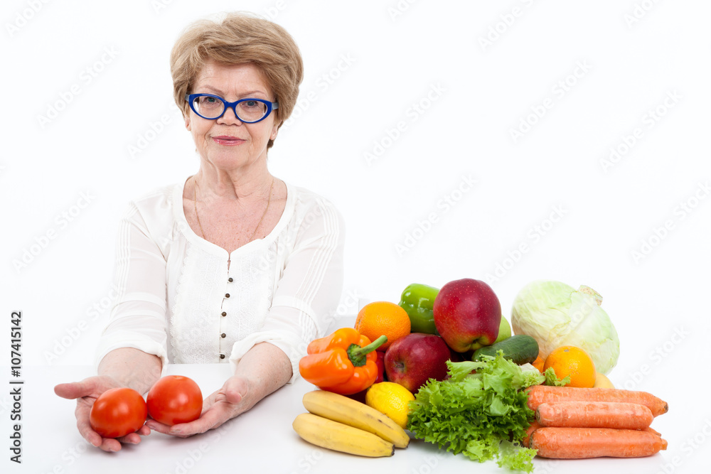 Woman retirement age with two tomatoes in hands sitting near fresh fruit and vegetables, white background Woman retirement age with two tomatoes in hands sitting near fresh fruit and vegetables, white background