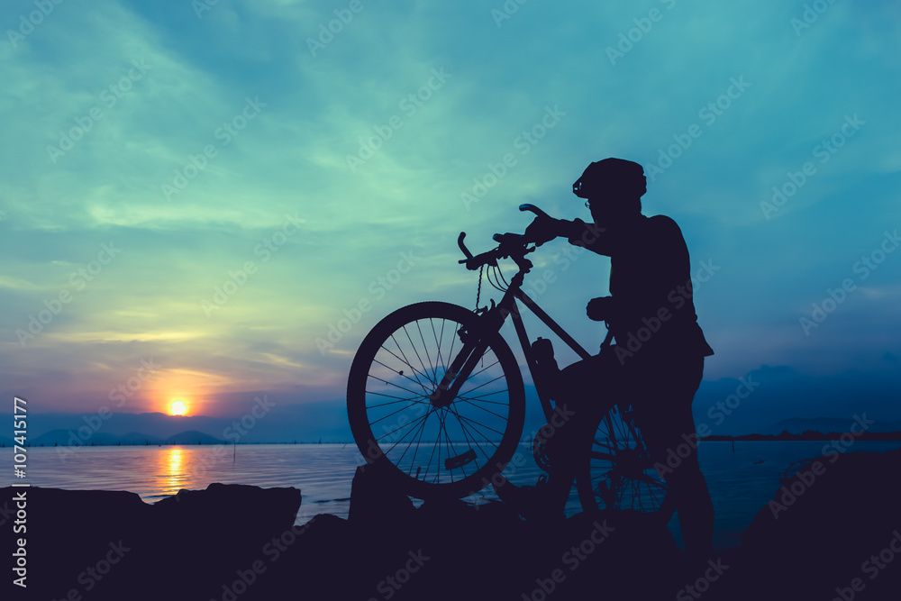 Obraz premium Healthy lifestyle. Silhouette of bicyclist standing with bike at seaside