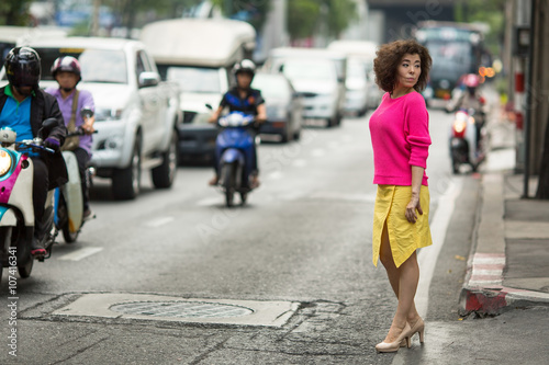 Young asian woman stands near a busy city highway.