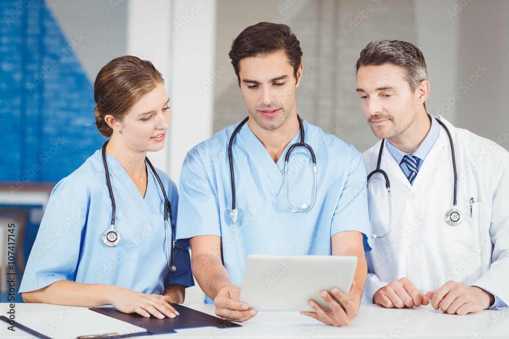 Doctor and colleagues using digital tablet while standing at desk in hospital Doctor and colleagues using digital tablet while standing at desk in hospital