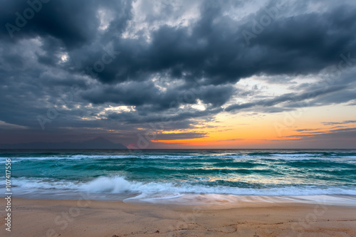 Sea and sandy beach with dramaric sky at sunrise