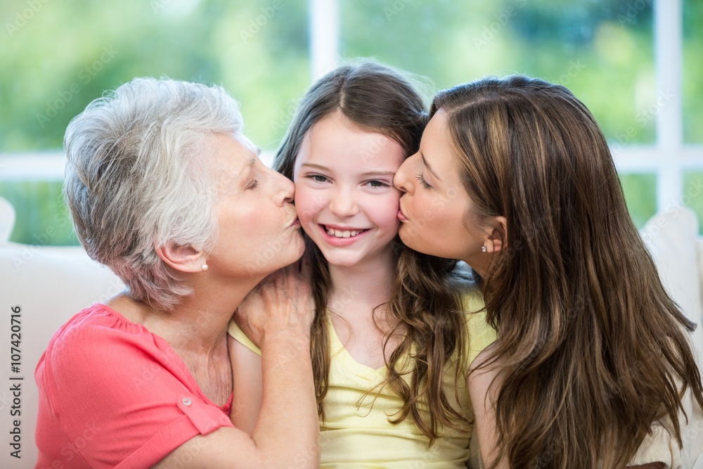 Mother and grandmother kissing happy girl on sofa