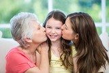 Mother and grandmother kissing happy girl on sofa