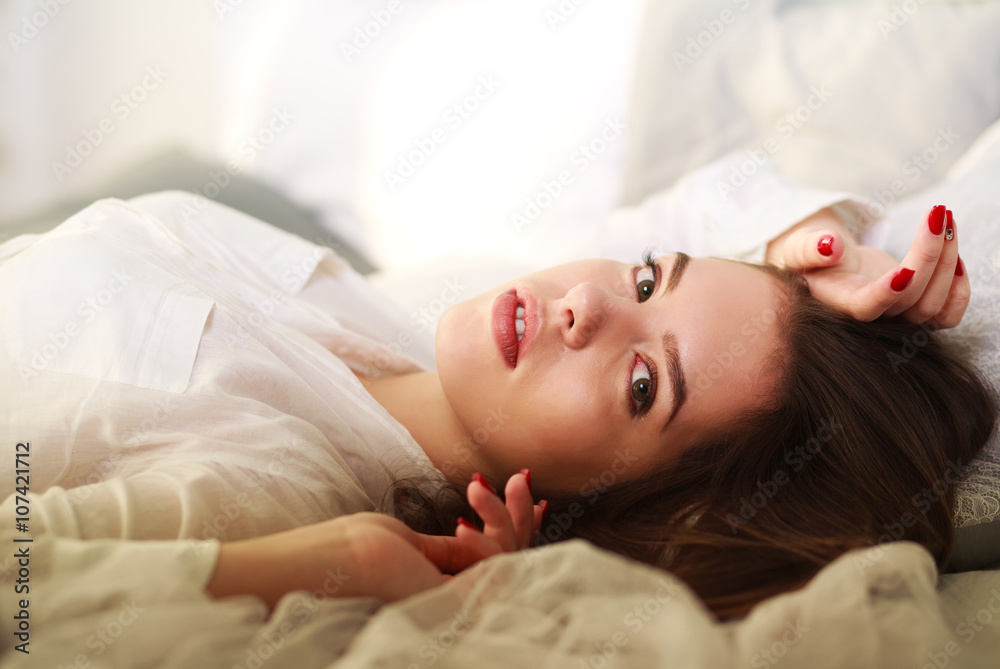 Fototapeta premium Beautiful thoughtful girl lying in bed on background of sunlight