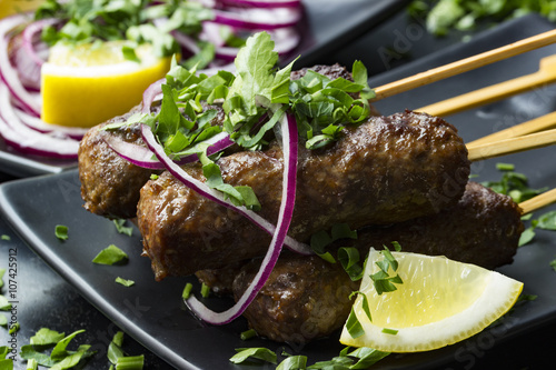 Cevapcici am Holzstick mit Petersilie und Zitronenschnitz auf einem Teller photo