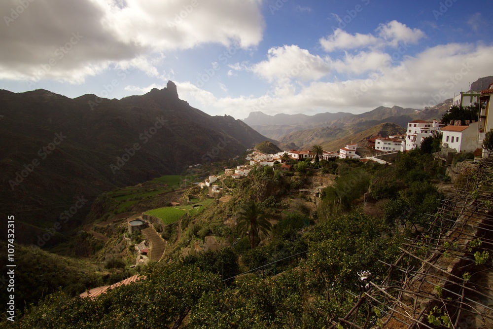 Mountain small village with foggy mountains, hills and rock monument on the background. Spring. Spain - Gran Canaria.