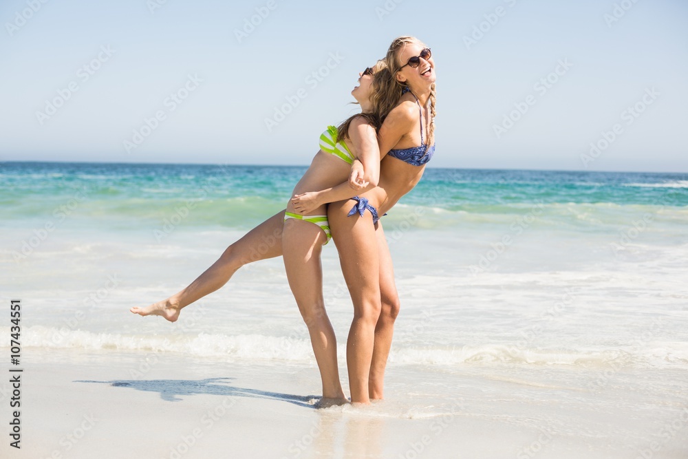Two happy women in bikini and sunglasses having fun on the beach