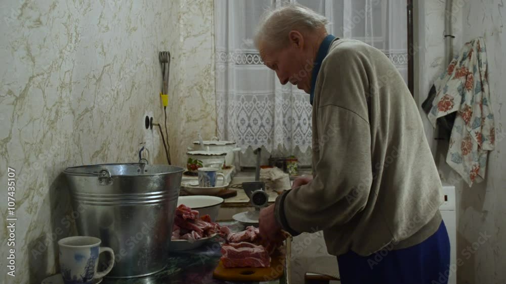 an Elderly Man With a Knife Cut Meat Into Small Pieces in Kitchen an Elderly Man With a Knife Cut Meat Into Small Pieces in Kitchen