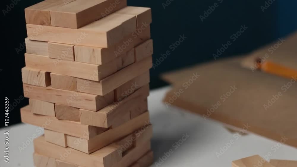Closeup hand girl take one block on the tower from wooden blocks, dark tone.