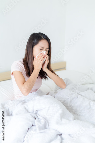 Woman sneezing and sitting on bed