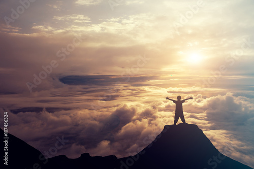 A boy standing on the top of the mountain above the clouds. Succ