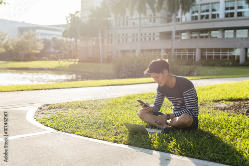 Korean man using laptop and cell phone in grass photo