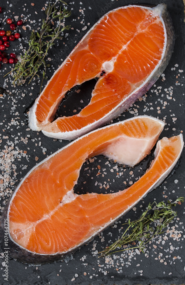 Two fresh raw salmon or trout steaks with salt, peppers and thyme Two fresh raw salmon or trout steaks with salt, peppers and thyme