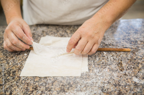 Hands baking dough with rolling pin on wooden table