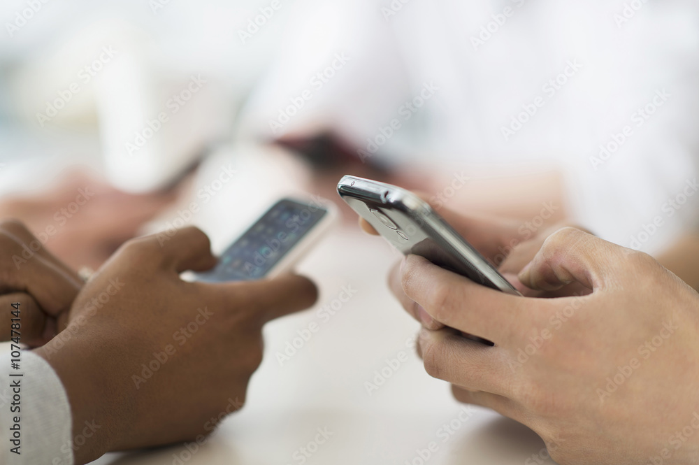 Close up of friends texting with cell phones at table Close up of friends texting with cell phones at table