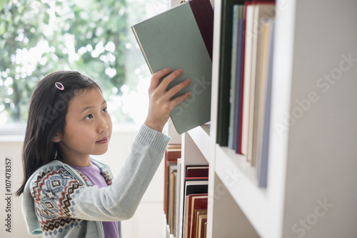 Chinese student selecting book from library bookcase